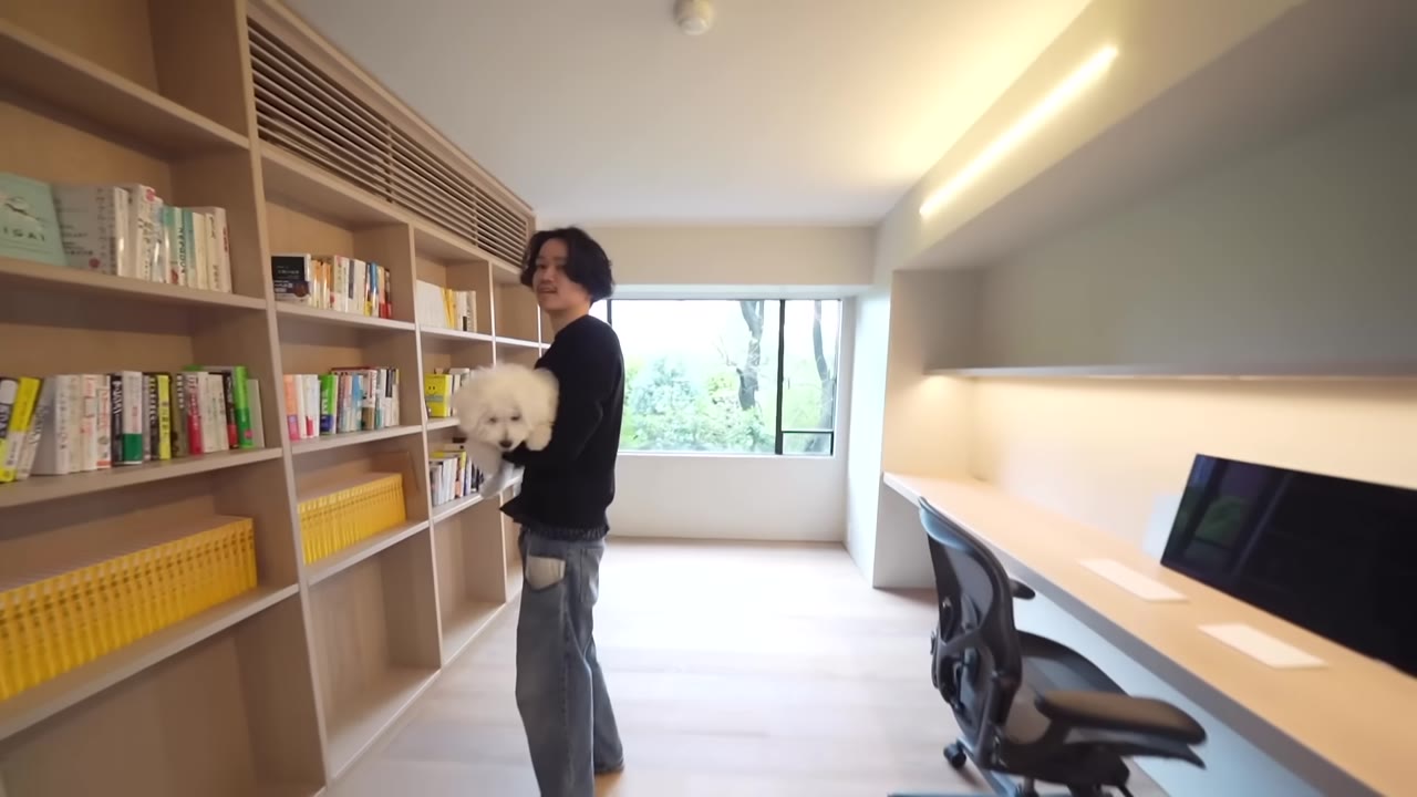 間接照明が入った長い本棚の壁と、犬を抱く八木さん