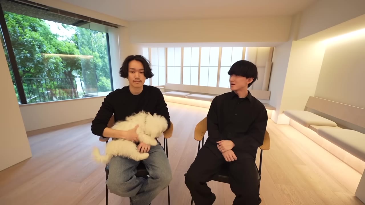 窓を背に椅子に座り、犬を抱いて話す2人